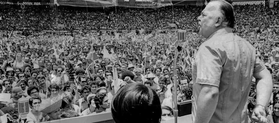 Juan Mari Brás habla ante una multitud que ondea banderas puertorriqueñas en un estadio